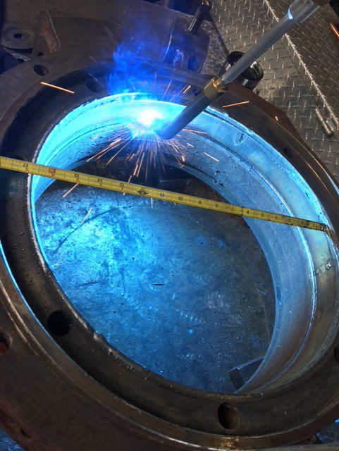 Welding a large metal circular structure with a measuring tape beside it.
